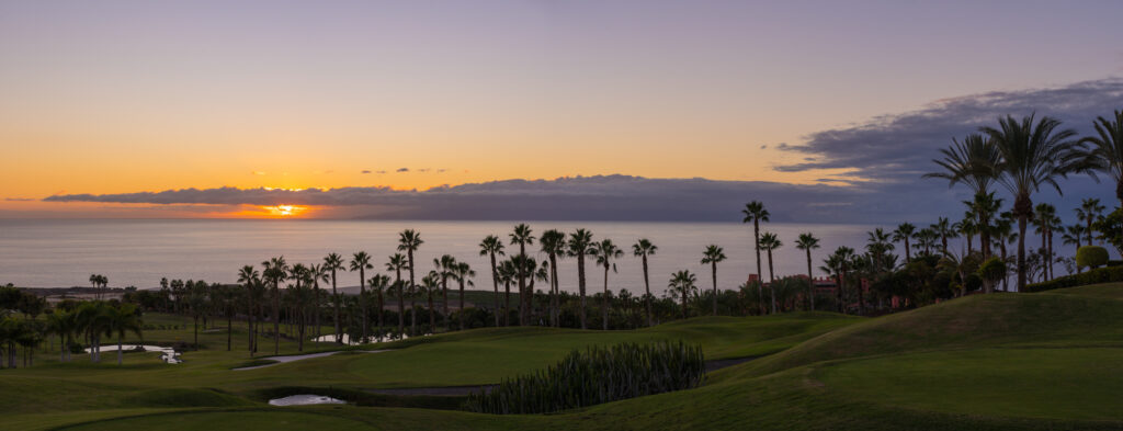 Fairway with bunkers, water hazards and trees around at Abama Golf Course with ocean view at sunset