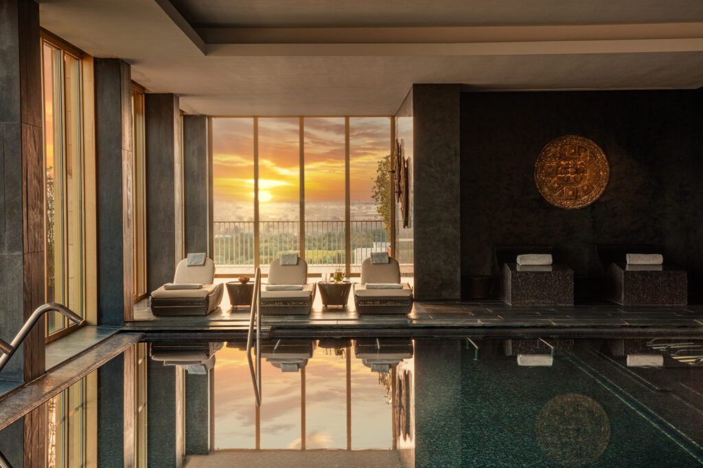 Indoor pool with spa beds and sunset in the background at Anantara Vilamorua