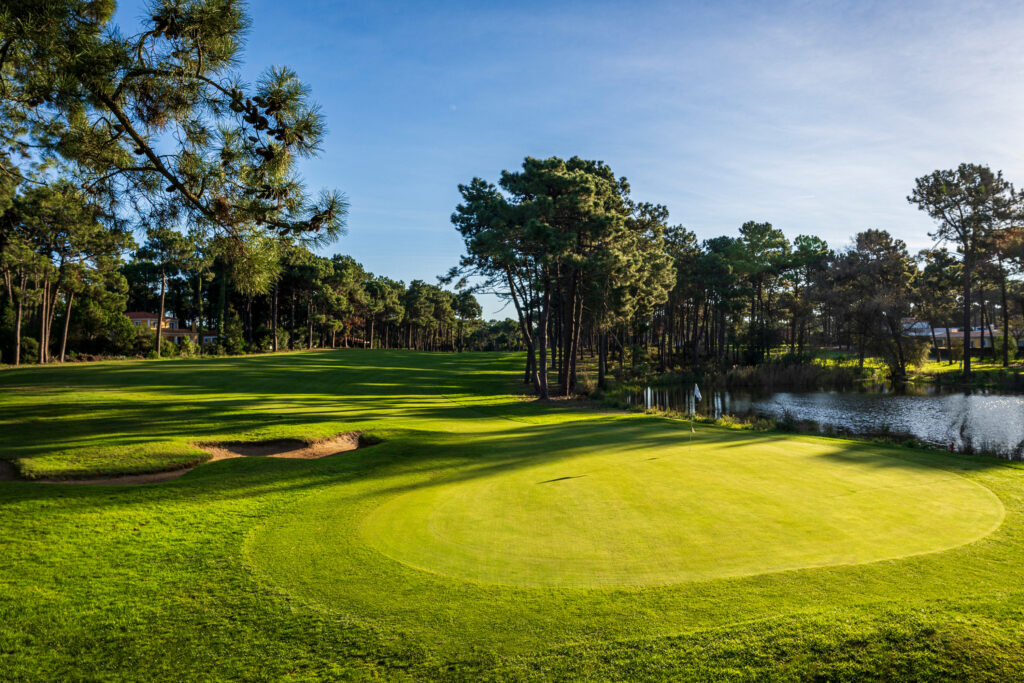 A hole with trees around and a lake at Aroeira Challenge Golf Course