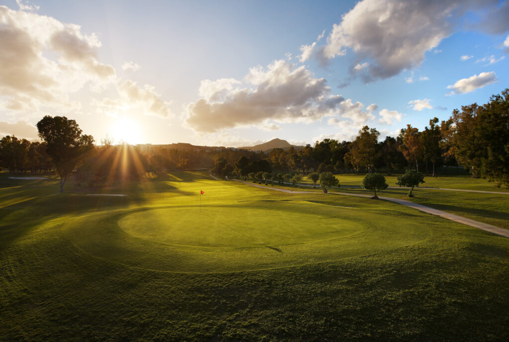 Hole with red flag with trees around with sun shining at Atalaya - Old Golf Course