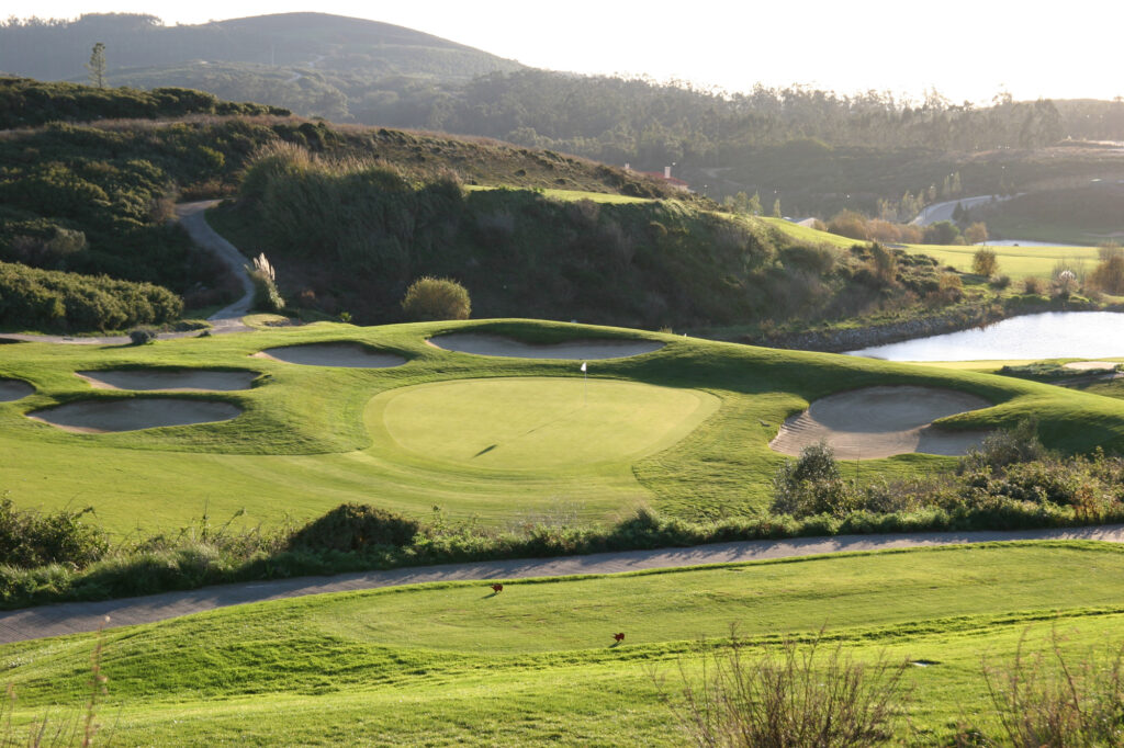 A hole surrounded by bunkers with hills in the background at Belas Clube de Campo Golf Course