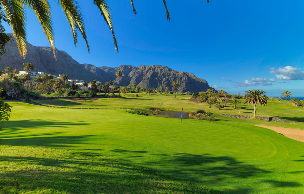 Hole with water hazard and trees around at Buenavista Golf Course with mountains in distance