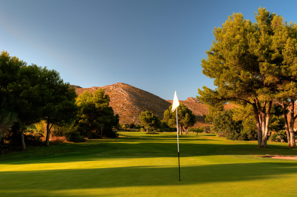 Hole with white flag with hills in background at Capdepera Golf Course