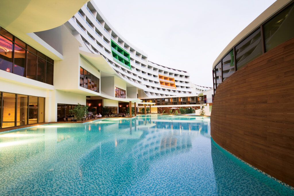 A shallow pool in the foreground & the hotel surrounding the outside area's of close to the pool