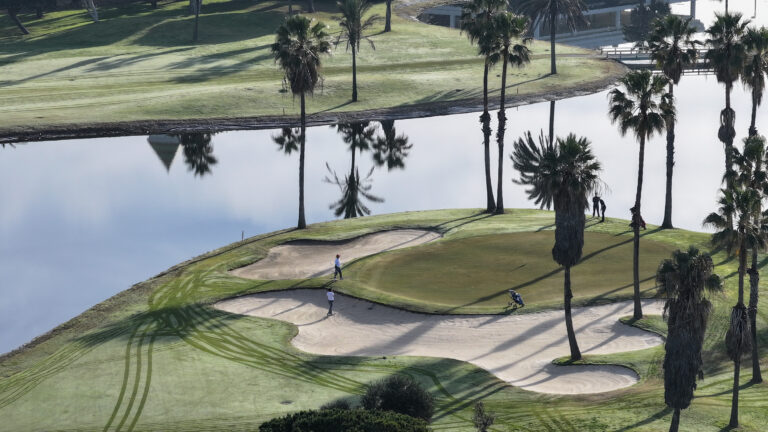 People playing golf on a green with bunkers and a lake nearby at Costa Ballena Ocean Golf Club