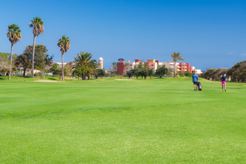 People playing golf at Fuerteventura Golf Club with trees around and building in background