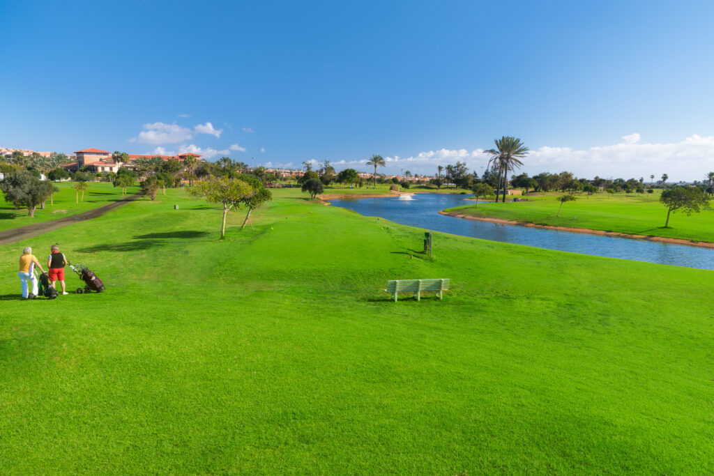 Fairway with people playing golf with trees in background at Fuerteventura Golf Club with a river running through