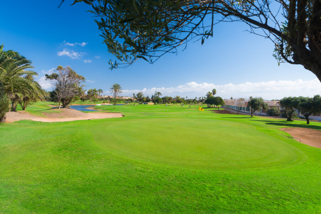 Hole with yellow flag with bunker and trees around at Fuerteventura Golf Club