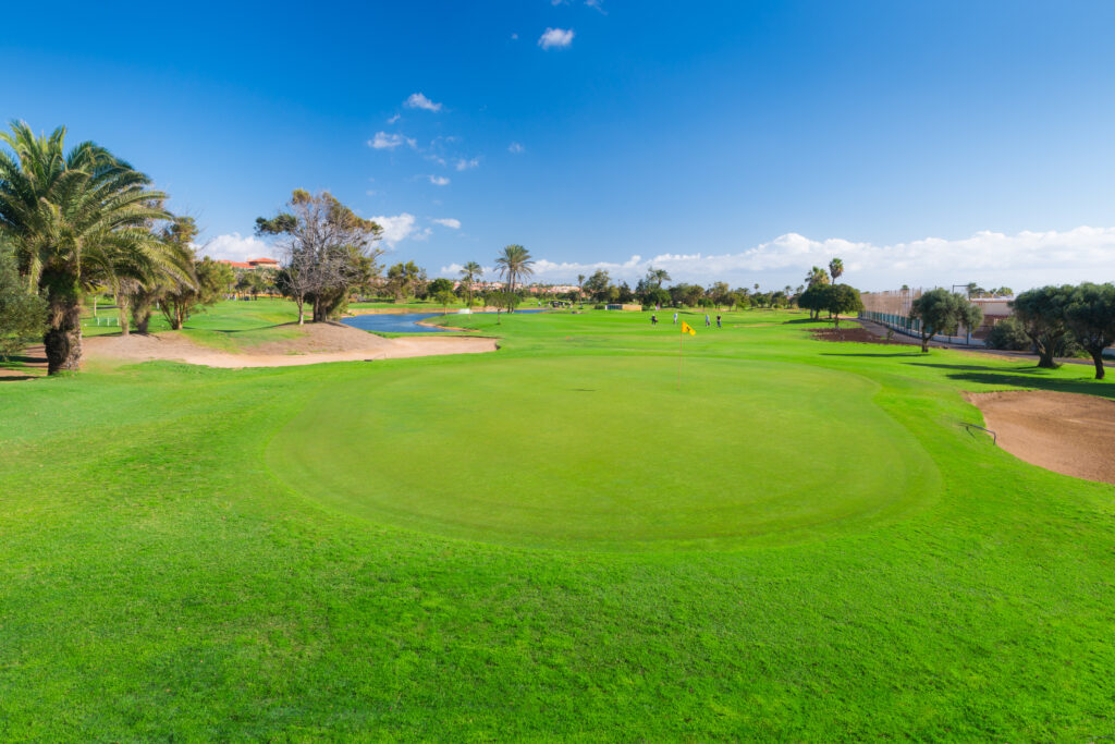 Hole with yellow flag with bunker and trees around at Fuerteventura Golf Club