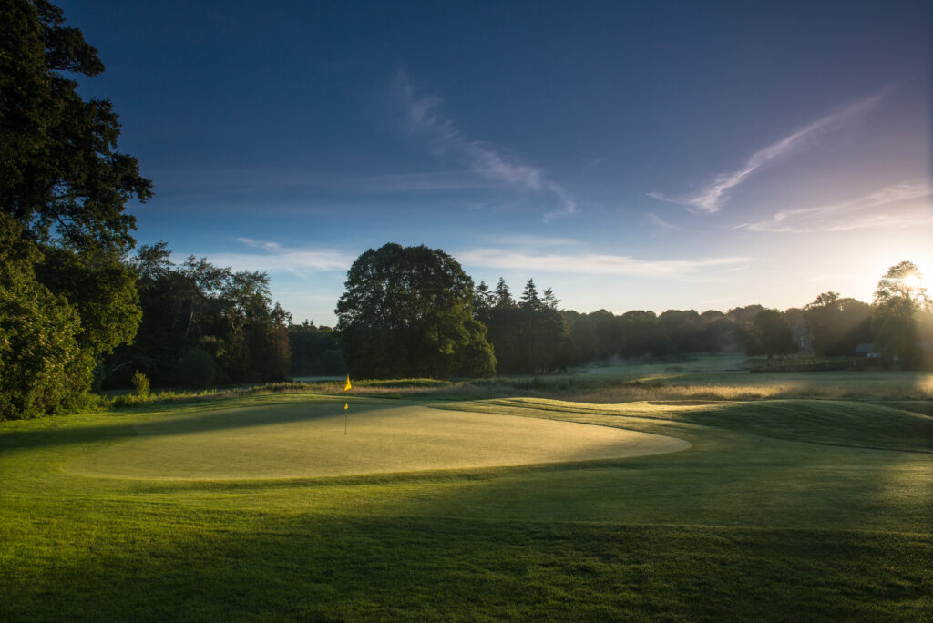 Hole with yellow flag at Galgorm Championship Course with trees around