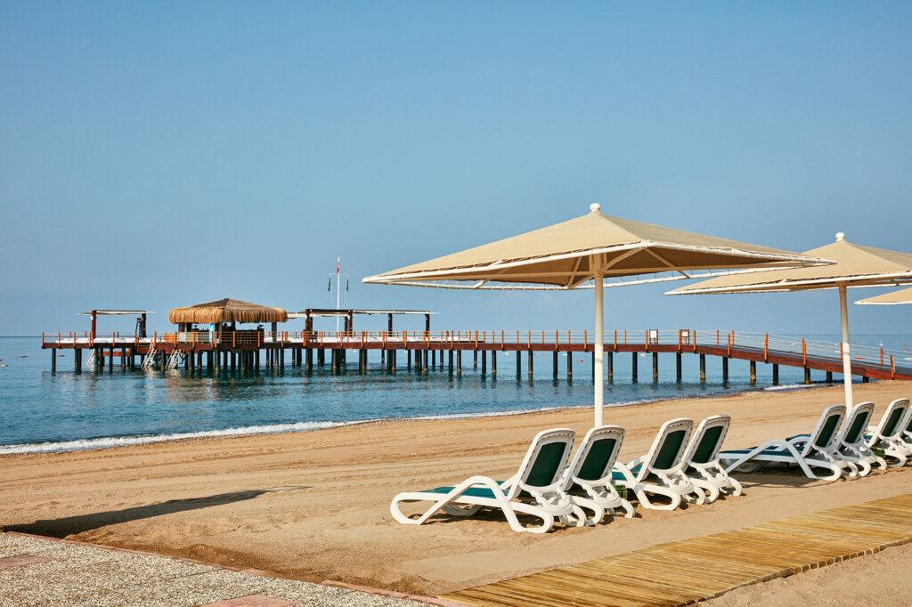 View of the golden sandy beach, with a view out to a small wooden pier where guests can enjoy watersports