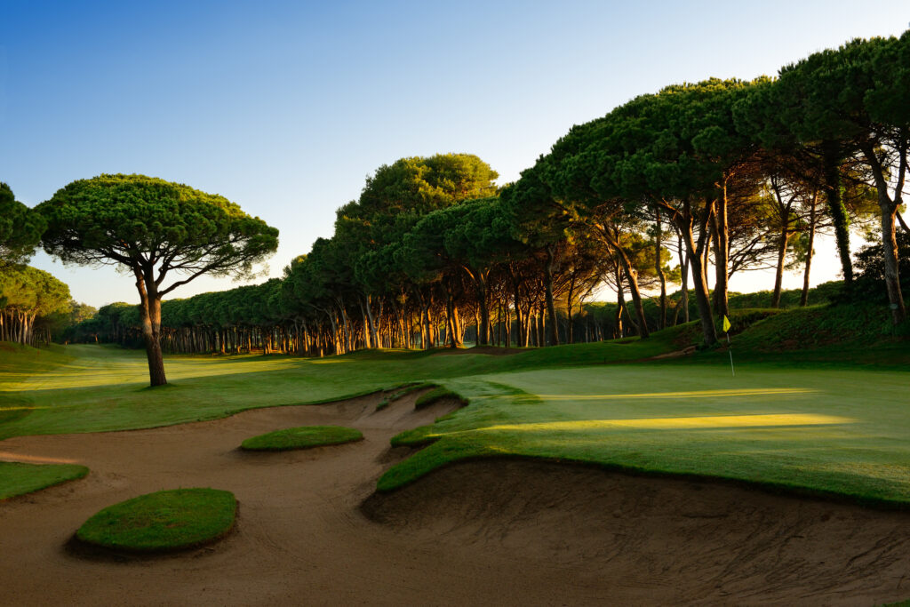 Fairway with bunker and trees around with a hole with a yellow flag at Golf de Pals Course