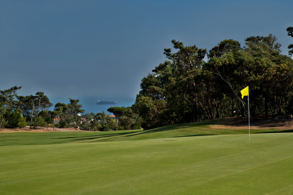 A hole with trees and ocean in the background at Golf do Estoril Golf Course