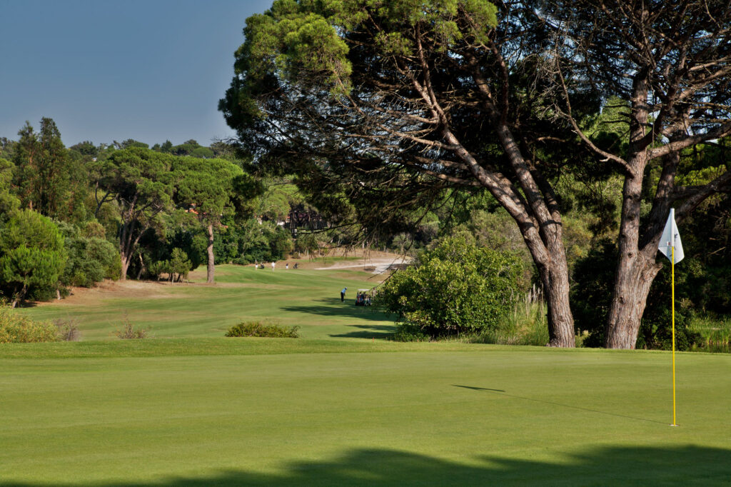 Hole with trees around and people playing golf in the background at Golf do Estoril Golf Course