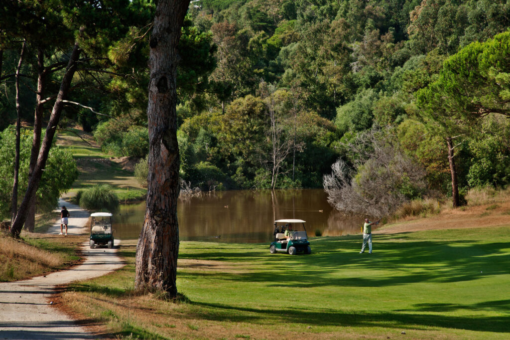 People playing golf with a buggy at Golf do Estoril Golf Course with a lake in the background