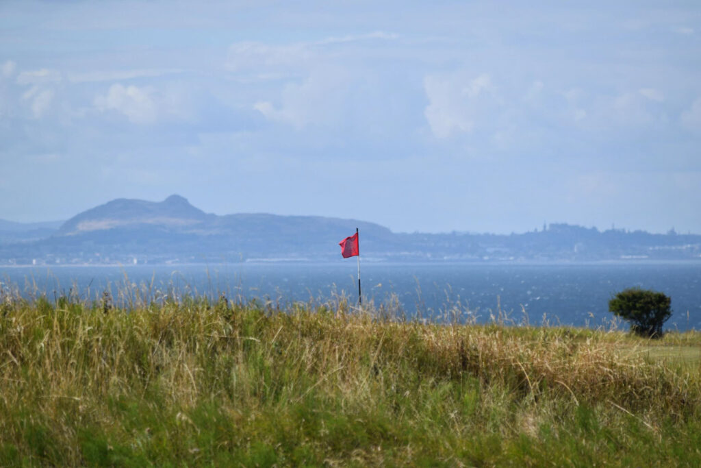 Hole with red flag at Gullane Golf Club - No. 2 Course with ocean in background