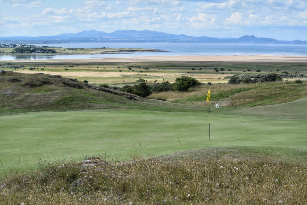 Hole with yellow flag at Gullane Golf Club – No. 3 Course with ocean in background