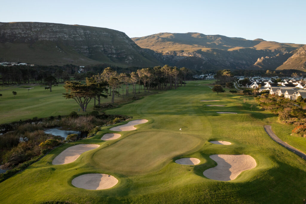 Hole with bunkers around at Hermanus Golf Club with trees and mountains in background