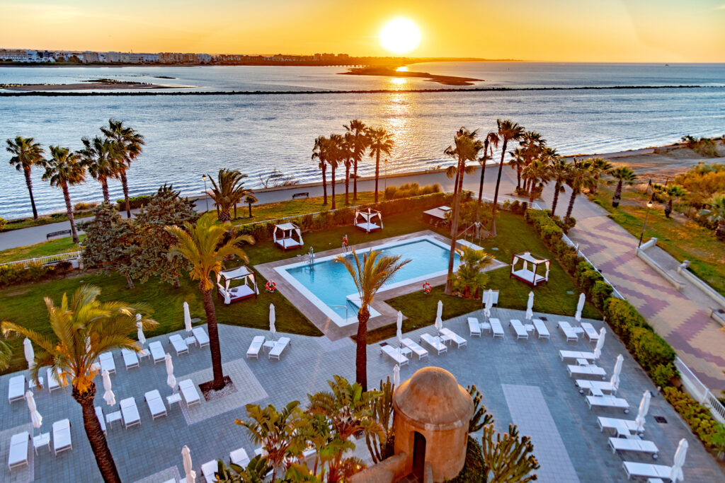 Aerial view of outdoor pool with ocean view at Hotel Melia Isla Canela at sunset