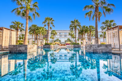 Outdoor pool with palm trees at Hyatt Place Taghazout Bay with hotel exterior in background