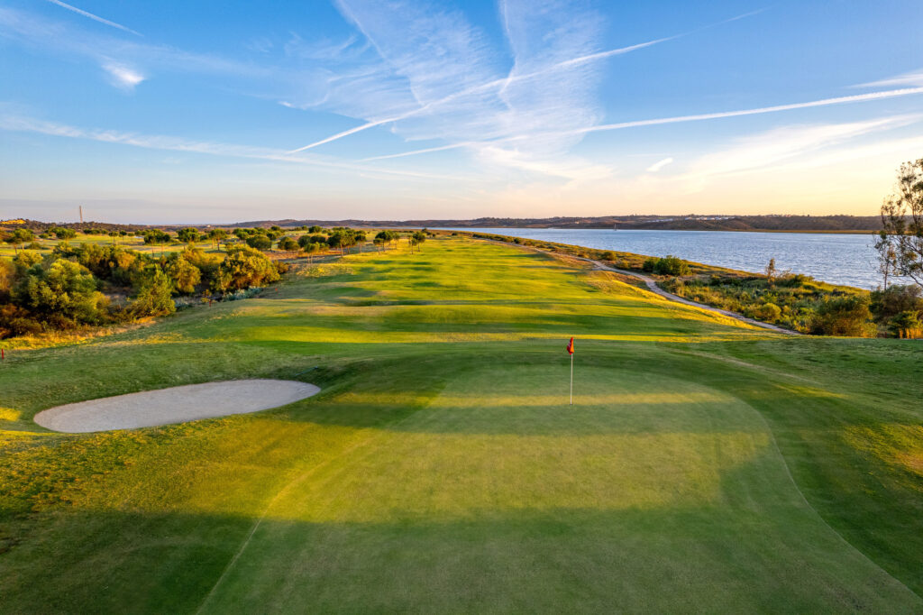 Hole with red flag with fairway in the background and a lake nearby at Isla Canela Links