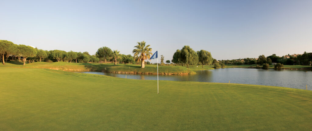 Hole with blue flag and lake in background at Pinheiros Altos Golf Course with trees around