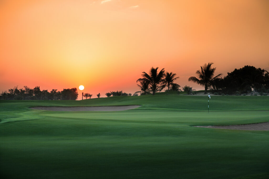 Hole with bunkers nearby at Abu Dhabi Golf Club - National with trees in background at sunset