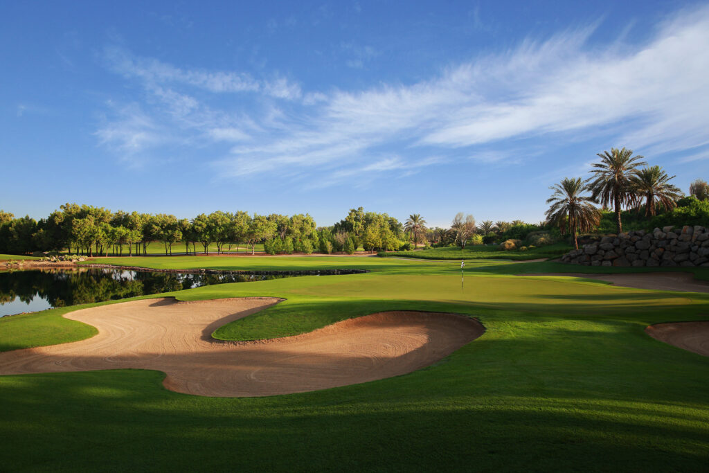 Hole with bunker at Abu Dhabi Golf Club - National with trees in background