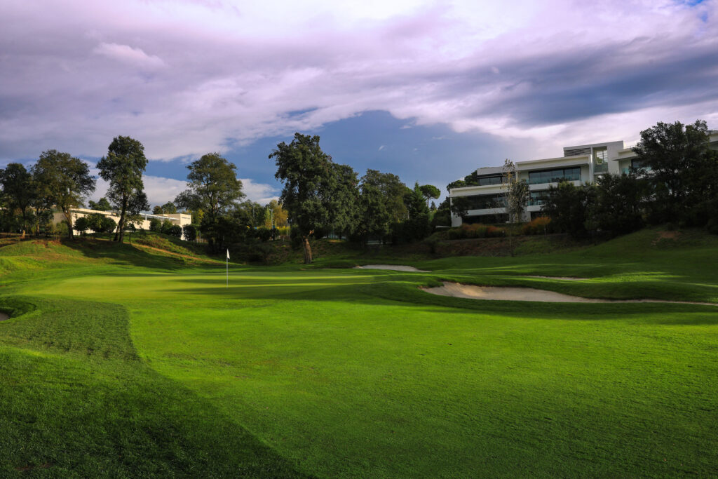 Fairway with a hole with white flag and building in the background at Camiral Golf & Wellness - Stadium Course