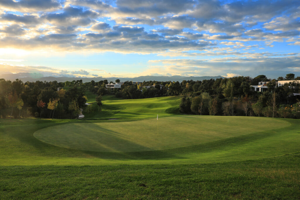 A hole with a white flag at Camiral Golf & Wellness - Tour Course with the fairway surrounded by trees