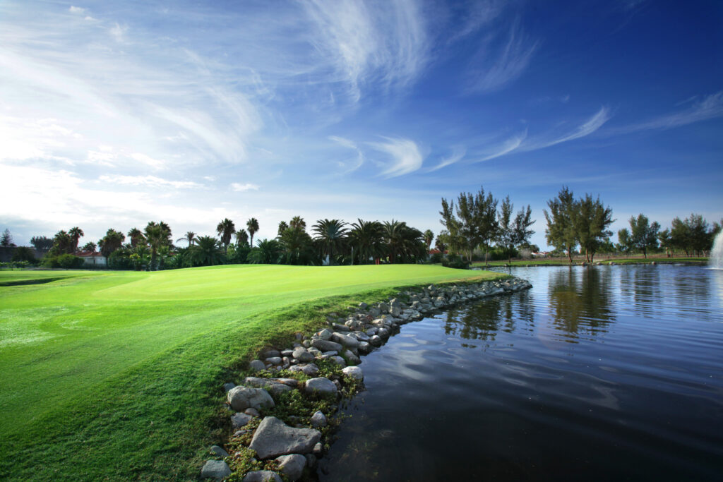 Hole with lake around at Campo de Golf de Maspalomas with trees in background