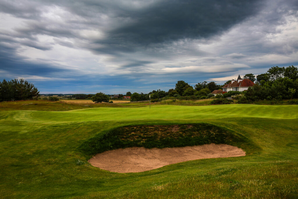 Hole with bunker at Craigielaw Golf Club with building in background and trees around