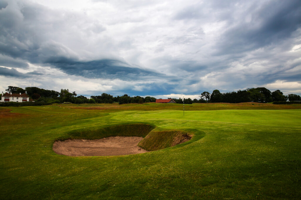 Hole with bunker at Craigielaw Golf Club with trees and building in background