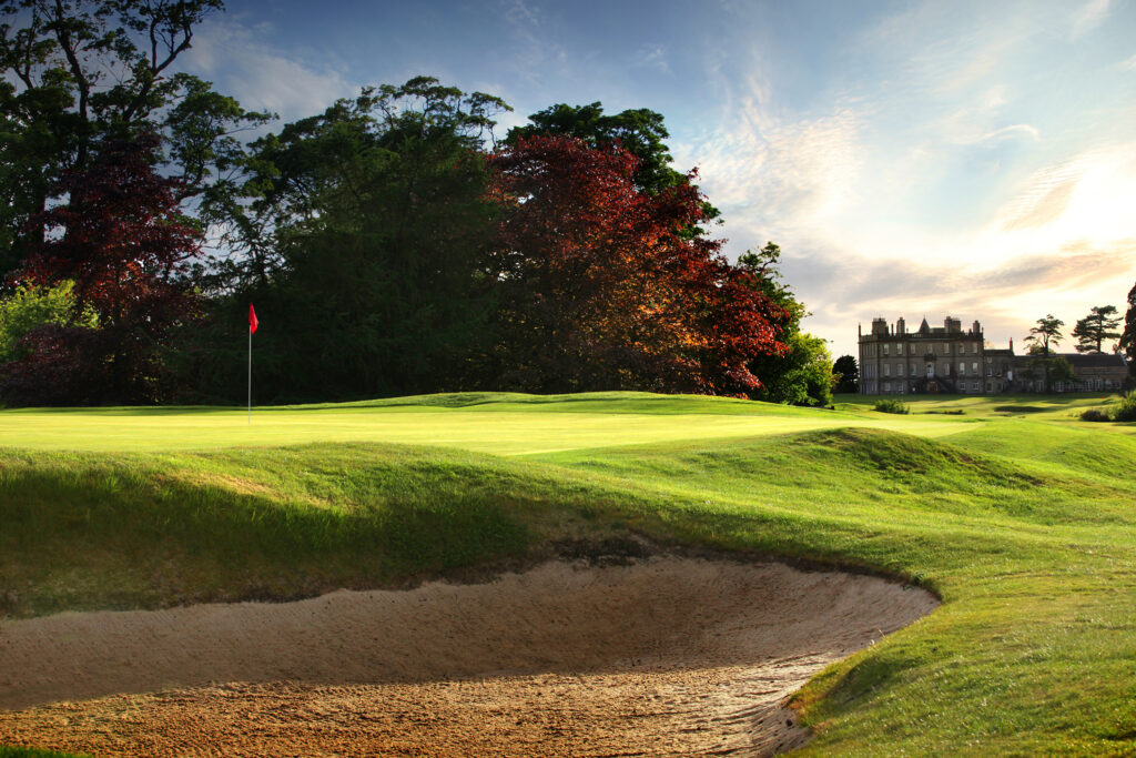 Hole with red flag and bunker at Dalmahoy - East Course with building in distance