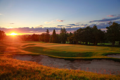 Hole with bunkers around at The Dukes Course with trees around at sunset