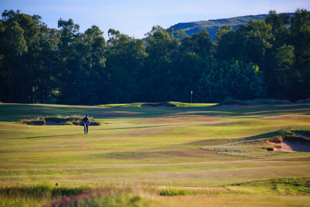 Person playing golf at The Dukes Course with trees around