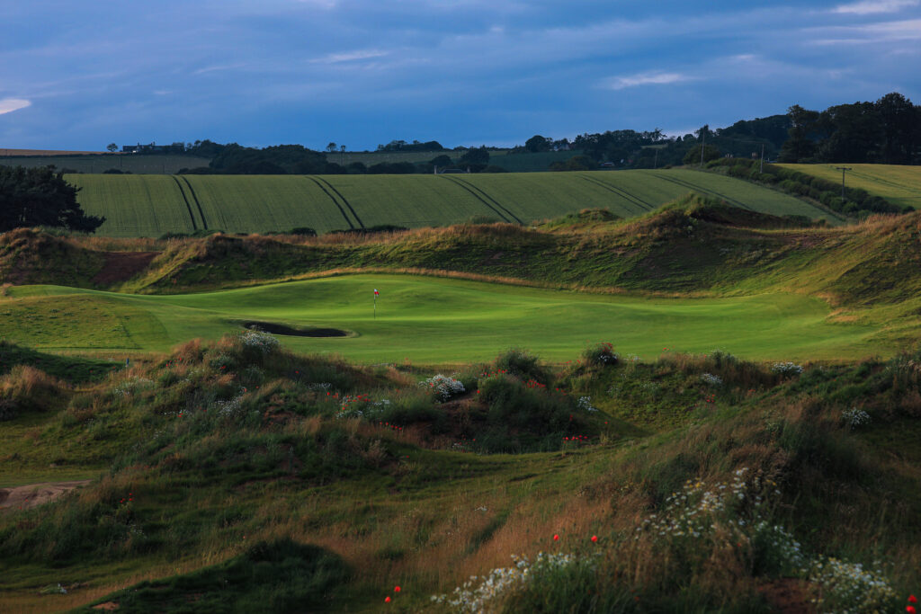 Hole with bunker at Dumbarnie Links with trees and hills in background