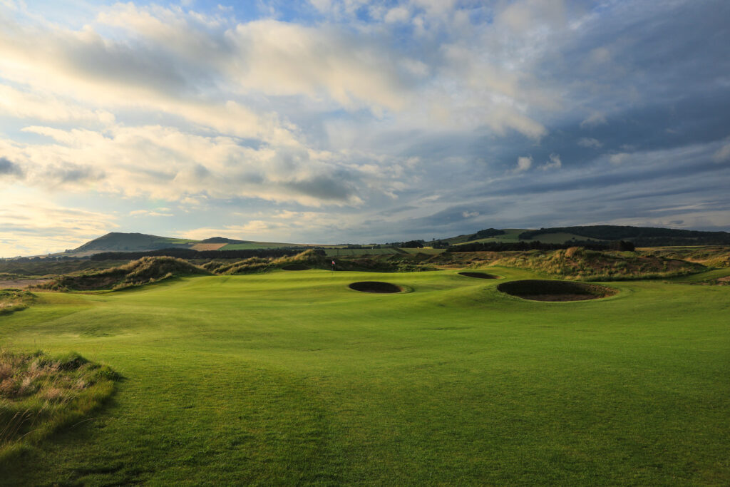 Hole with bunkers at Dumbarnie Links with hills in background