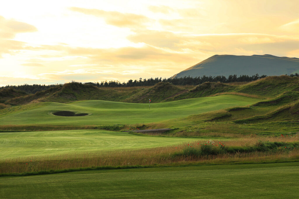 Hole with bunker at Dumbarnie Links with hills and trees in background