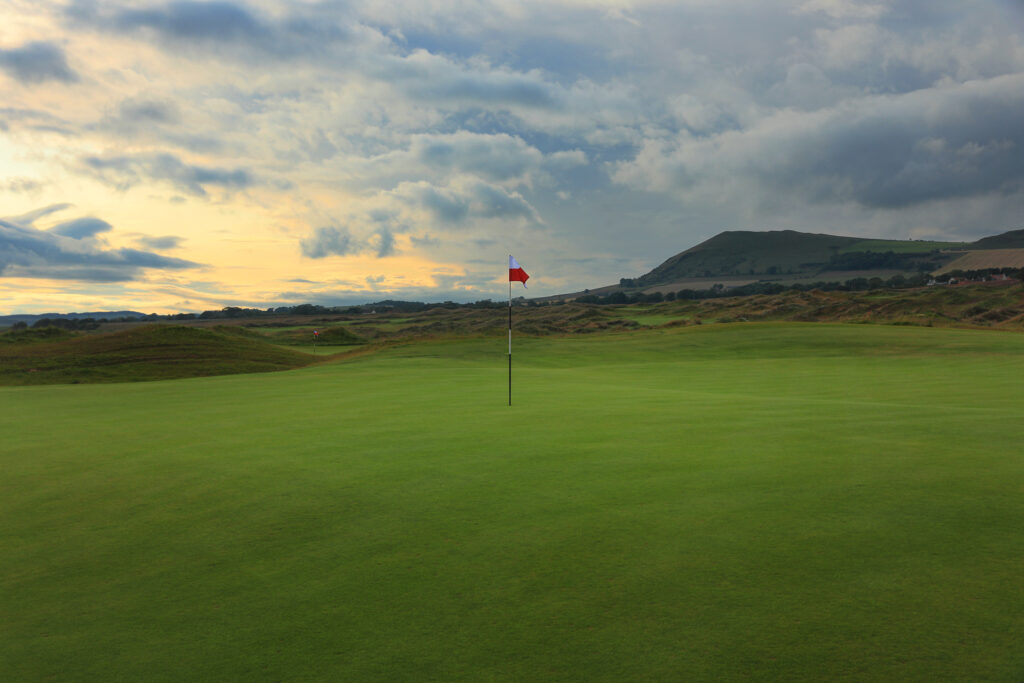 Hole with white and red flag at Dumbarnie Links with hill in background