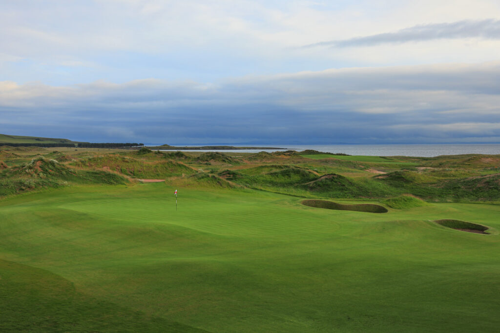 Hole with bunkers at Dumbarnie Links with ocean in backgroud