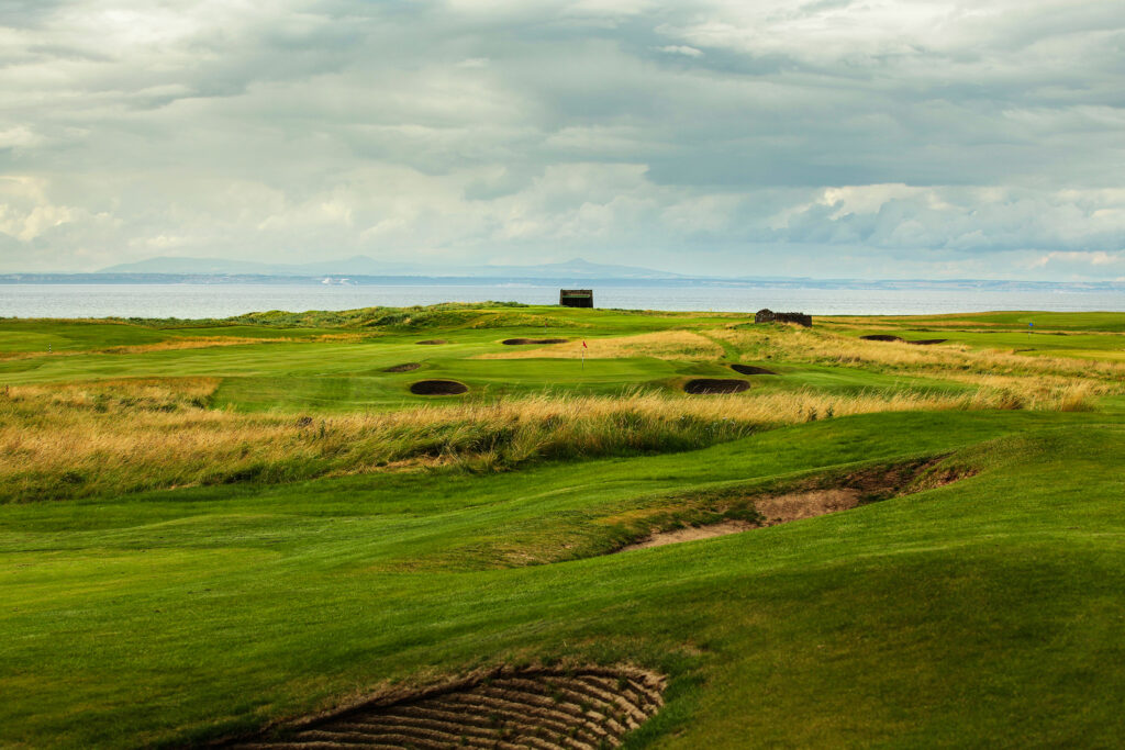 Fairway at Kilspindie Golf Club leading to hole with red flag and bunkers at Kilspindie Golf Club with ocean in background