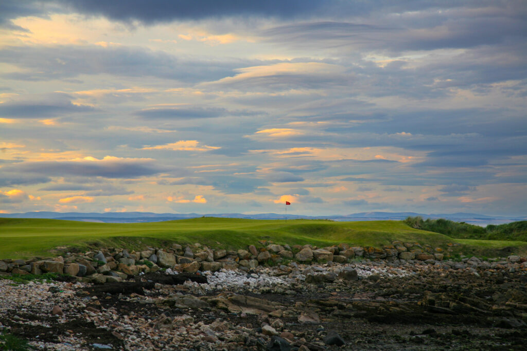 Hole with red flag at Kingsbarns Golf Links with rocks in foreground