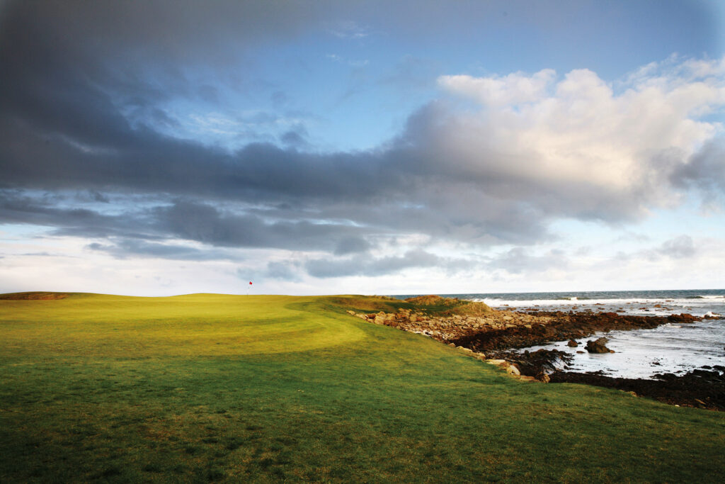 Hole with red flag at Kingsbarns Golf Links next to the ocean