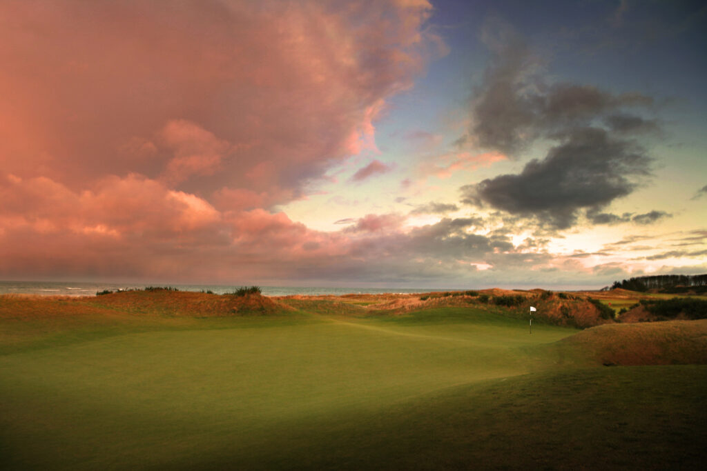 Hole with white flag at Kingsbarns Golf Links at sunset