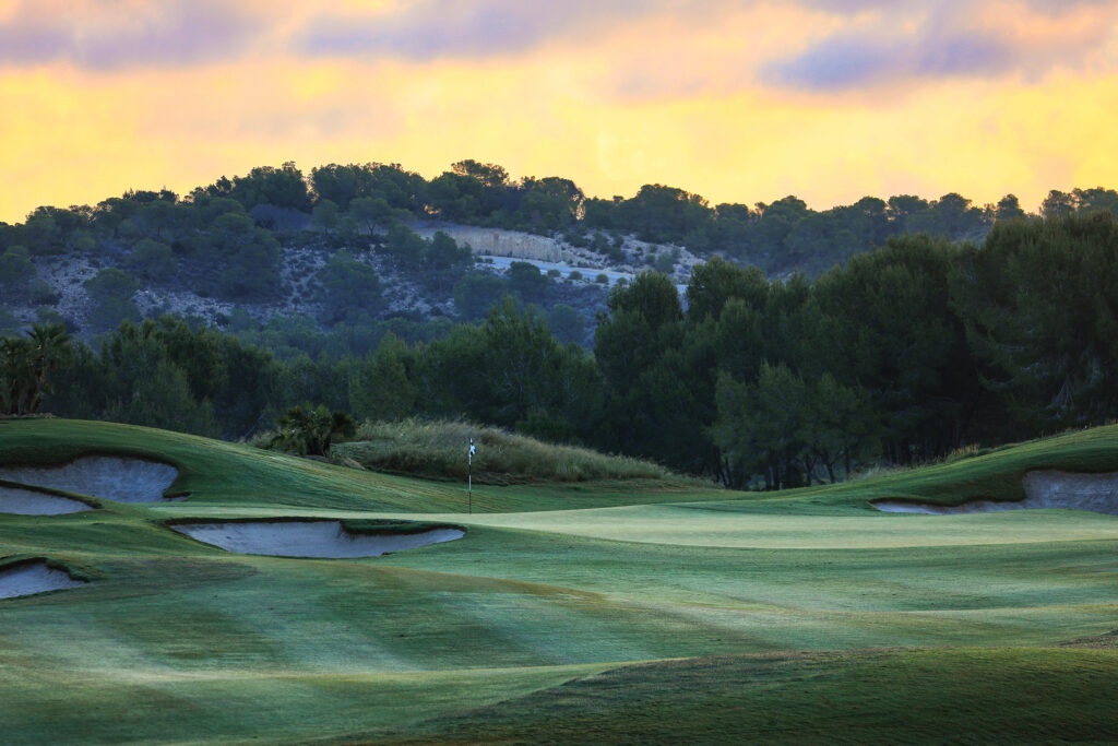 A hole with bunkers and a hill in the background at sunset at Las Colinas Golf & Country Club