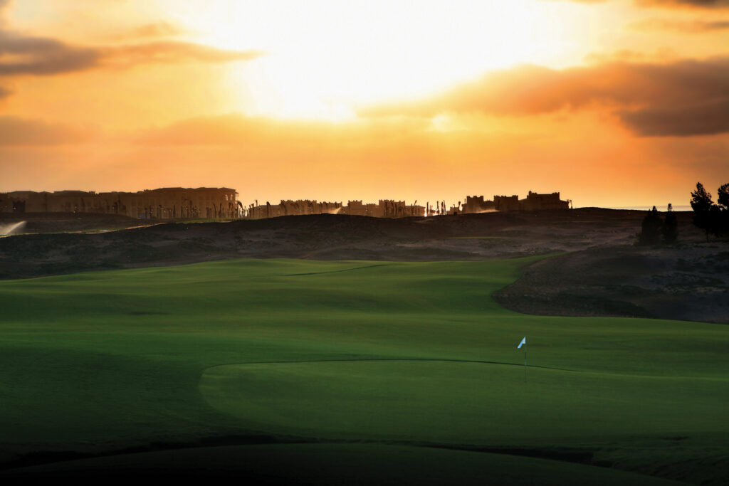 Hole at Mazagan Golf Course with buildings in distance at sunset