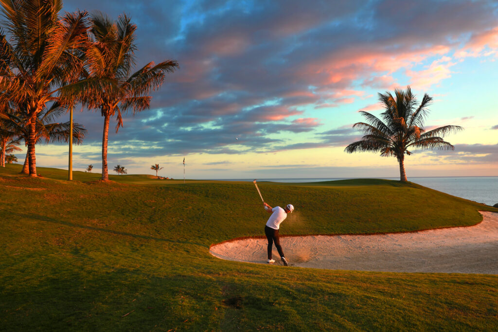 Person playing golf in bunker with trees around at sunset at Meloneras Golf