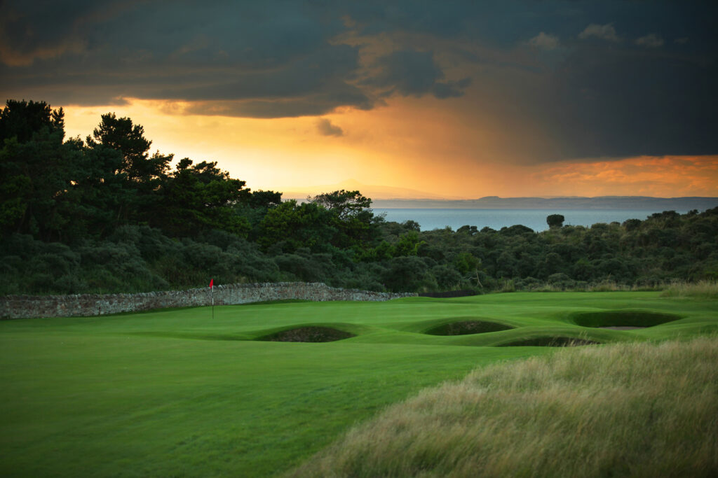 Hole with red flag and bunkers at Muirfield with trees around