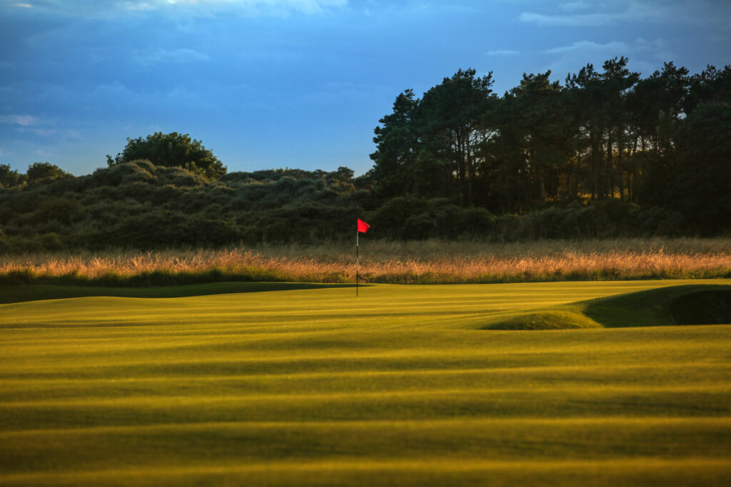 Hole with red flag at Muirfield with trees in background